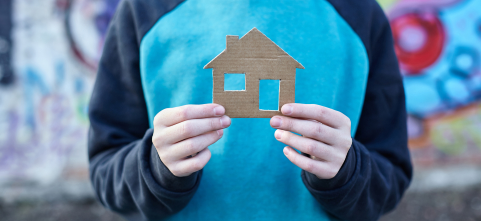 Faceless person wearing blue hoodie and holding cardboard house. 