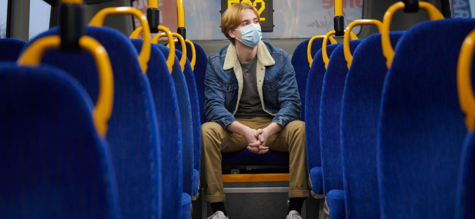 En dreng sidder alene i en bus med mundbind på.