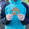 Faceless person wearing blue hoodie and holding cardboard house. 